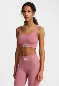 Roze geribbelde sportcrop-top met brede bandjes, gecombineerd met hoge geribbelde leggings. Beide hebben een klein merklabel op de taille.