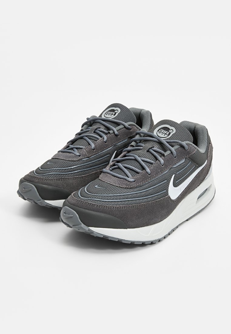 Baskets Nike Air Max avec un dessus en daim gris et en mesh, des lignes de design ondulées distinctes, un système de laçage, un logo blanc et une semelle rembourrée.