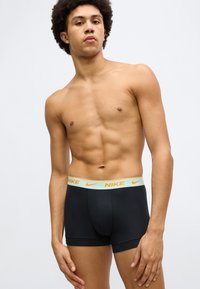 Mustad puuvillased bokserid, millel on mündiroheline vöökoht ja oranž Nike logo. Keha järgiva lõikega ja sileda tekstuuriga.