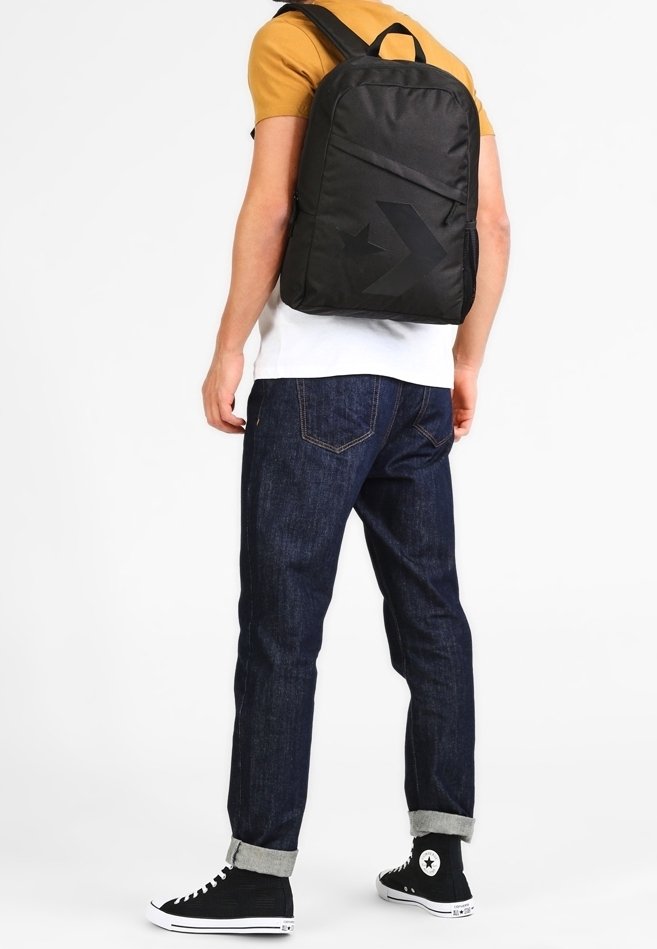 Sac à dos noir avec une surface en tissu lisse, de forme rectangulaire et un grand accent graphique. Sangles attachées et une poignée supérieure pour le transport.