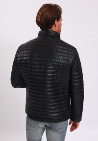 Giacca di pelle nera con design trapuntato, dotata di collo alto e una superficie liscia. Il retro presenta dettagli di cuciture orizzontali.