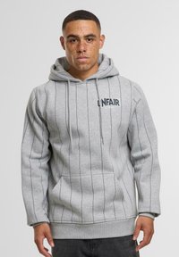Felpa grigia con strisce nere verticali, tasca frontale e cappuccio regolabile con cordoncino. Presenta il logo "UNFAIR" sul lato sinistro del petto. Texture morbida.
