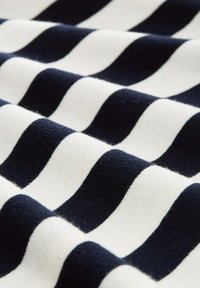 Tissu tricoté avec des rayures ondulées alternées en bleu marine foncé et blanc, présentant une surface texturée et un aspect doux.