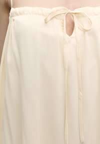 Robe crème sans bretelles avec un col froncé et un petit trou en forme de clé noué d'un fin nœud en tissu sur la poitrine.