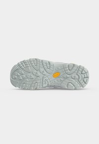 Semelle d'une chaussure de randonnée grise avec des rainures profondes et un logo Vibram orange au centre sur un fond blanc uni.