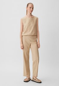 Beiges ärmelloses Top kombiniert mit passenden, taillierten Hosen und lässigen braunen Sandalen. Der Stoff wirkt weich mit einer strukturierten Oberfläche.