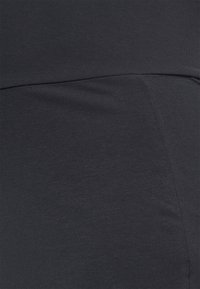 Detailní záběr na tmavě šedou látku s viditelným prošíváním a hladkou texturou, ukazující detaily švů oděvu.