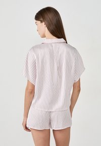 Korte mouwen lichtroze pyjama set met verticale dunne rode strepen. Het topje heeft een kraag en een losse pasvorm; de shorts zijn vergelijkbaar in ontwerp.