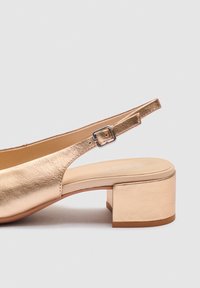 Metallisk guld slingback sandal med blokhæl, justerbar spænde og polstret indersål på neutral baggrund.