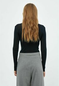 Melna garām piedurknēm izgatavota no mīksta auduma, apvienota ar gaiši pelēkiem piegriezuma biksēm. Iespējojot pieguļošu dizainu un eleganti plānu siluetu.