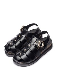 Sandalias de cuero negro con diseño de tiras entrecruzadas, punta abierta y tira trasera con hebilla dorada. Plantilla de corcho texturizada y suela negra.