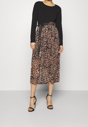 Schwarzes langärmeliges Oberteil kombiniert mit einem knielangen Rock mit Leopardenmuster, der eine gebundene Taille und schwarze Akzente aufweist. Stilettabsätze vervollständigen den Look.