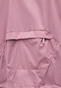 Εμπρόσθια όψη τσέπης ανοιχτό μωβ μπουφάν με καπάκι και μικρή υφασμάτινη ετικέτα με την ένδειξη "Salomon" στην επάνω άκρη.