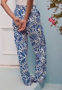 Valkoiset pellavahousut, joissa on sinisiä kukka- ja geometrisia kuvioita. Housuissa on rento malli, joustava vyötärönauha ja sivutaskut.