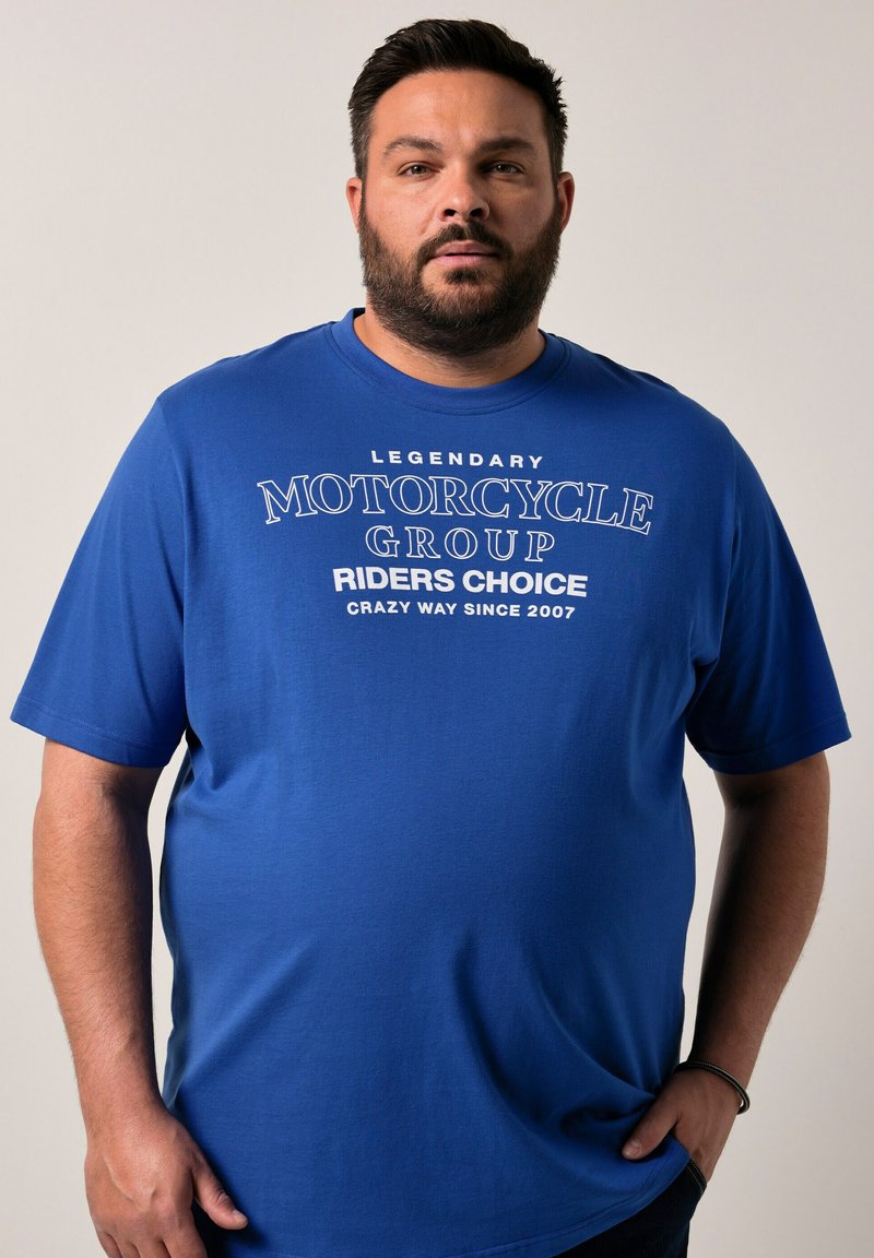 Modrá tričko s krátkým rukávem vyrobené z bavlny, se bílým potiskem textu: "LEGENDÁRNÍ MOTOCYKLOVÁ SKUPINA VOLBA JEZDCŮ ŠÍLENÝ ZPŮSOB OD ROKU 2007."