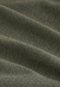 Grüner Stoff mit einer weichen, strukturierten Oberfläche, die feine Strickmuster zeigt und mit natürlichen Falten und Schatten fällt.