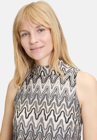 Top bez rękawów z wysokim dekoltem, z falistym wzorem w kolorach czarnym, beżowym i białym. Teksturowany materiał z widocznymi detalami szycia.