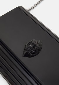 Czarna kopertówka o błyszczącej powierzchni z misternym, teksturowanym akcentem czarnego pióra z przodu. Posiada metalowy łańcuszek do noszenia.