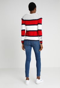 Pull rayé rouge, blanc et bleu marine avec un motif en maille texturée et un col côtelé, associé à un jean skinny bleu et des baskets blanches.