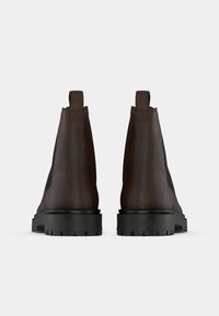 Botine din piele maro, cu finisaj texturat, panouri laterale elastice și talpă din cauciuc negru cu un model de tread robust.