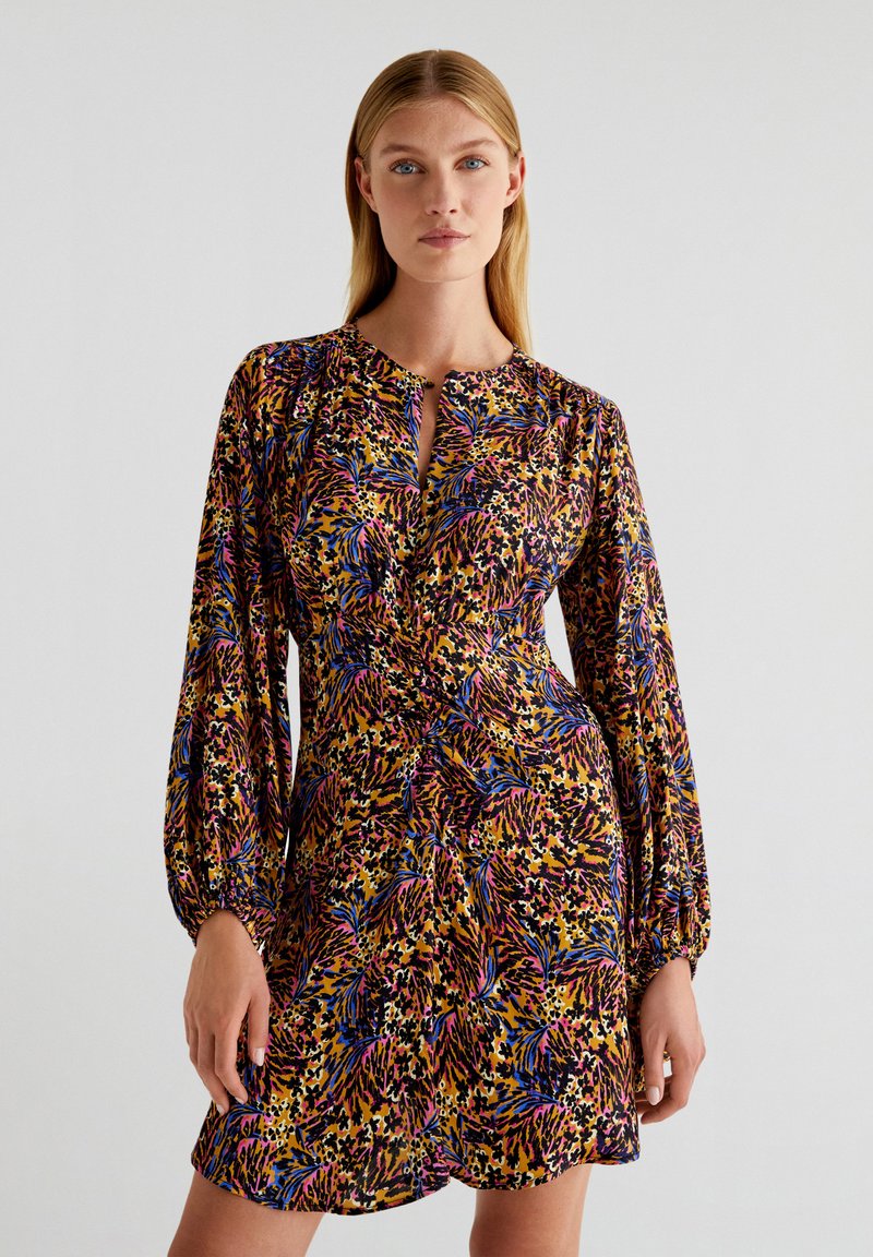 Robe à motif floral dans des teintes vives de violet, jaune et rose. Dotée de longues manches bouffantes et d'un décolleté en forme de trou de serrure.