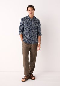 Sinine mustriga särk valgete lehemotiividega, pika varrukaga, varrukad üles keeratud, koos helepruunide linast pükstega ja tumedate pruunide sandaalidega.