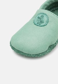 Mintgrön lädersko med slip-on-design, texturerad ovandel och en mjuk mockaliknande sula. Den har en cirkulär logotyp på framdelen och sydda detaljer.