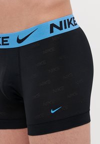 Sorte boksertruser med teksturert stoff, med en blå elastisk midjebånd med "NIKE"-merke og en liten blå logo på benet.