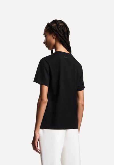 T-shirt nera in cotone con maniche corte, scollo rotondo e piccolo dettaglio con logo sul retro. Tessuto liscio, design aderente.