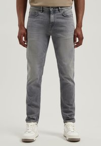 Szürke farmernadrág slim fit szabással, elhalványított mosással, klasszikus öt zsebes kialakítással és gombos záródással, fehér sportcipővel párosítva.