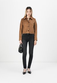Giacca cropped in suede marrone con chiusura a bottoni, due tasche frontali e colletto a punta, abbinata a jeans skinny neri e ballerine nere.