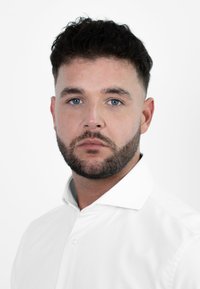 Man met kort donker haar en een baard, gekleed in een wit overhemd met knopen. De achtergrond is eenvoudig wit, waardoor het onderwerp benadrukt wordt.