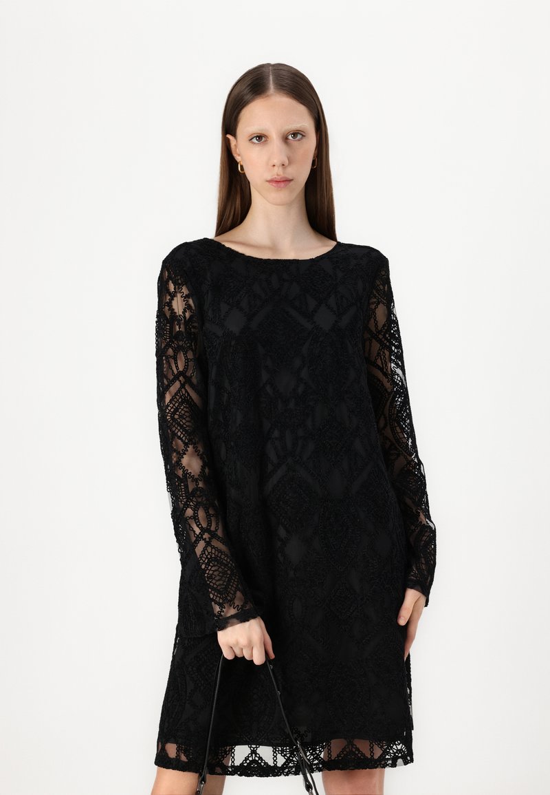 Vestido negro de encaje con mangas largas y transparentes, patrón geométrico, cuello redondo y corte holgado, con un dobladillo ondulado y textura detallada.