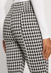 Högmidjade leggings med ett svart och vitt hundtandsmönster, tillverkade av elastiskt tyg med en slät yta.