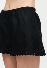 Μαύρο σορτς με ελαστική μέση και κεντήματα με λουλουδάτα μοτίβα στην άκρη, που φοριέται στο πάνω μέρος του μηρού.