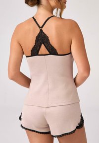 Jasnobeżowy zestaw do spania z prążkowanej tkaniny, ozdobiony czarną koronką, składający się z topu na ramiączkach i szortów, podkreślający fakturę oraz detale na krawędziach.