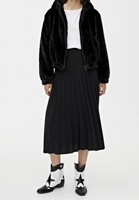 Black faux fur bomber jacket, white t-shirt, pleated black midi skirt, and black and white star-patterned cowboy boots.