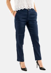 Pantaloni in blu navy, su misura, con una texture liscia, tasche frontali e chiusura a un bottone, abbinati a tacchi a punta neri.