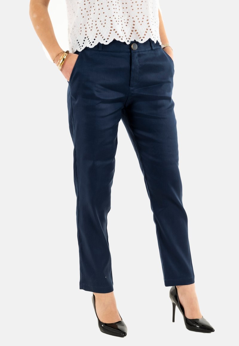 Pantaloni in blu navy, su misura, con una texture liscia, tasche frontali e chiusura a un bottone, abbinati a tacchi a punta neri.