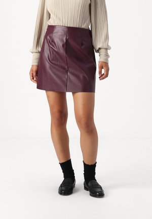 Mini spódniczka z burgundowej skóry o gładkim wykończeniu, z plisami z przodu. Dobierz ją do beżowego prążkowanego topu i czarnych mokasynów z krótkimi skarpetkami.