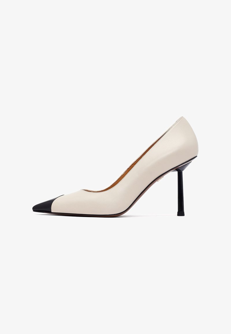 Beżowe skórzane czółenka z wąskim noskiem, czarnym noskiem oraz smukłym czarnym obcasem typu stiletto. Gładka faktura i minimalistyczny design.
