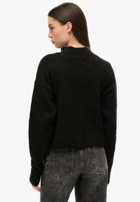 Un pull noir texturé avec un col rond et des épaules tombantes, associé à un jean noir délavé taille haute, vu de dos.