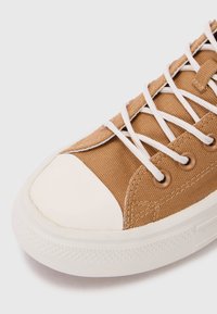 Bruine canvas sneakers met een witte rubberen neus, witte veters en metalen oogjes; gestructureerde bovenkant en een gladde zool.