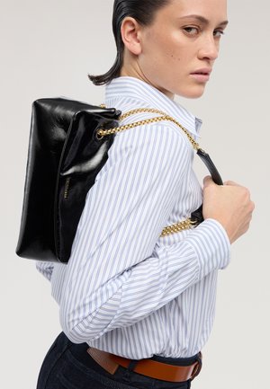 Czarny skórzany plecak o połyskującej fakturze, z paskami z łańcucha w kolorze złotym. Noszony na ukos, w połączeniu z niebiesko-białą koszulą w paski.