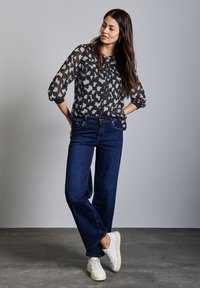 Průhledná blůza s černobílým vzorem a zapínáním na knoflíky, spárovaná s tmavě modrými volnými džínami a bílými teniskami. Hladké textury; ležérní střih.