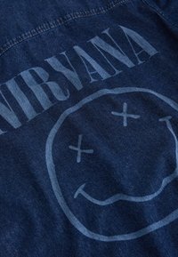 Tissu en denim avec une impression délavée du texte « NIRVANA » et un grand logo de visage souriant aux yeux barrés.
