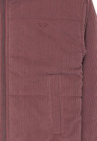 Burgundy corduroy zip-up jacket featuring vertical ribbed texture, side pocket, and small embroidered logo on the chest.