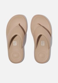 Beige teenslippers met een getextureerde band, voorzien van een gevoerde zool en subtiele logo-opdruk op de binnenzool. Eenvoudig, slank ontwerp.