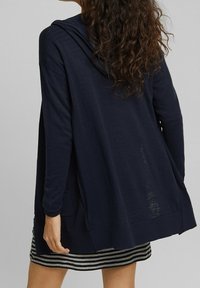 Navyblauwe lange mouwen cardigan met capuchon, relaxte pasvorm en open ontwerp. Voorzien van een zijzak en een textuurstof.