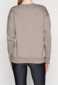 Hnědá mikina s volným střihem, spadlými rameny, žebrovanými manžetami a lemem. Měkký fleecový materiál, kombinovaný s černými legínami.